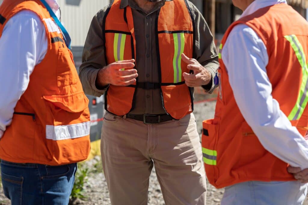 Engineers discussing project in orange vests.